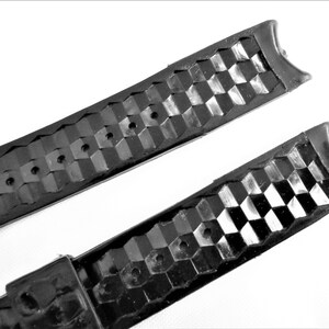 Puede incluir: Dos correas de reloj de goma negra con un patr&oacute;n texturizado a cuadros. Las correas tienen agujeros para ajustar el tama&ntilde;o.