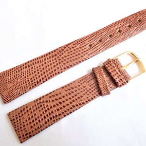 May include: A brown leather watch strap with a gold buckle. The strap has a textured, snake-like pattern.