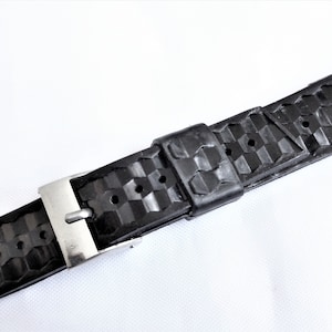 Puede incluir: Correa de reloj de caucho negro con hebilla plateada. La correa tiene un patr&oacute;n texturizado.