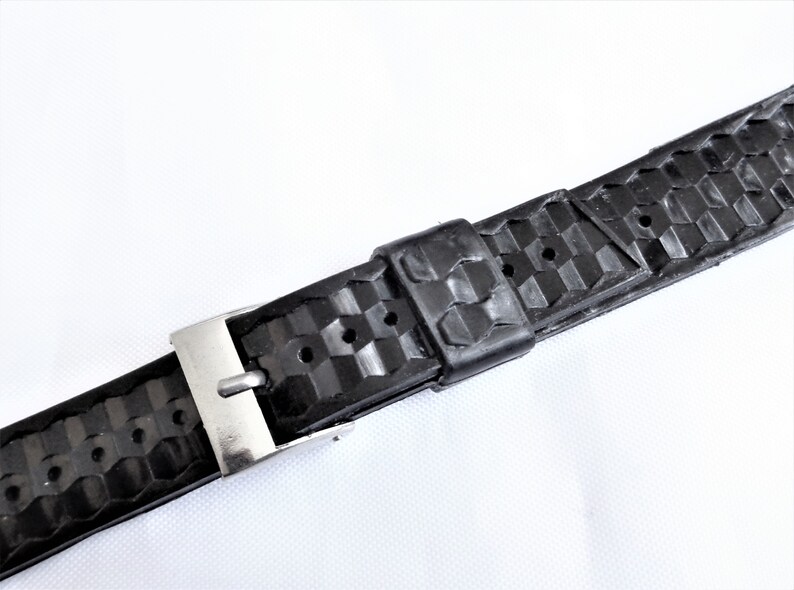 Puede incluir: Correa de reloj de caucho negro con hebilla plateada. La correa tiene un patr&oacute;n texturizado.