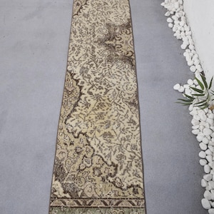 Pode incluir: Um tapete longo e retangular com fundo bege e um padrão floral castanho. O tapete tem uma borda verde e castanha.