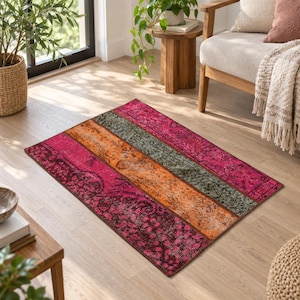 Può includere: Un tappeto rettangolare con un design patchwork a strisce orizzontali in tonalità vivaci di magenta, arancione brillante e verde oliva scuro, ogni sezione decorata con intricati motivi floreali e geometrici dall'aspetto sbiadito.