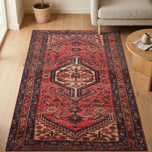 Può includere: Un tappeto rettangolare caratterizzato da uno sfondo rosso vivace con un motivo centrale a medaglione geometrico in blu navy e crema. Il tappeto è incorniciato da un bordo blu navy scuro decorato con intricati motivi floreali e di viti in rosso e crema.