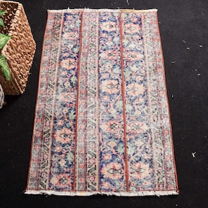 May include: A rectangular area rug featuring a vertical striped pattern with alternating bands of deep blue, faded pink, and muted green floral motifs. The rug has a distressed texture, thin orange dividing lines, and short white fringe at both ends.