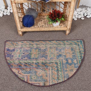 May include: A half-round rug with a colorful, geometric pattern in shades of blue, green, orange, and brown. The rug has a fringed edge and is made of a woven material.