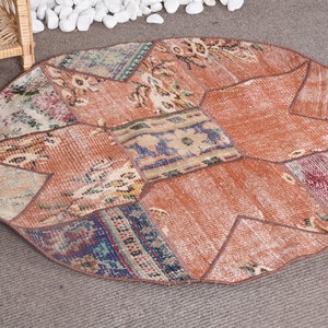 Könnte beinhalten: Ein runder Patchwork-Teppich, der aus verschiedenen Textilsegmenten in Terrakotta-, Rost-, Blau- und Cremetönen besteht. Der Teppich weist eine geometrische Anordnung genähter Stoffstücke mit verblassten Blumen- und abstrakten Mustern auf.