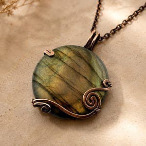 May include: A round labradorite pendant featuring a dark green and gold iridescent surface, secured by a copper wire wrap with decorative spiral accents. The pendant hangs from a dark copper-toned metal chain, showcasing a polished finish.