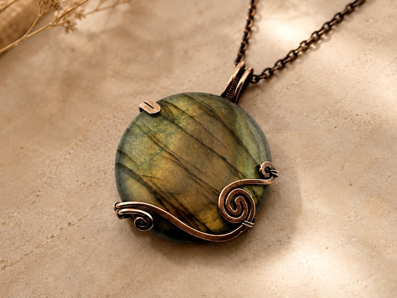 May include: A round labradorite pendant featuring a dark green and gold iridescent surface, secured by a copper wire wrap with decorative spiral accents. The pendant hangs from a dark copper-toned metal chain, showcasing a polished finish.