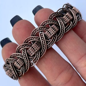 May include: A copper wire bracelet with a woven knot design. The bracelet is made of multiple strands of copper wire that are woven together to create a intricate pattern.