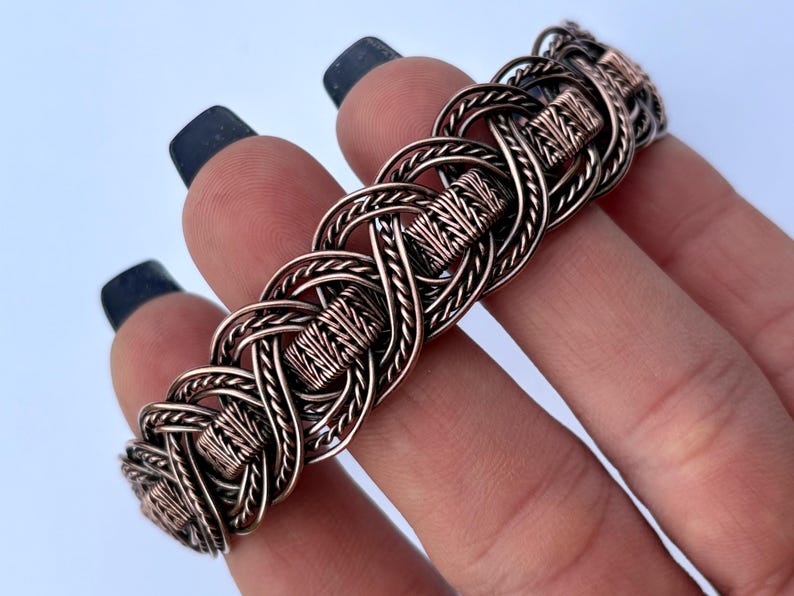 May include: A copper wire bracelet with a woven knot design. The bracelet is made of multiple strands of copper wire that are woven together to create a intricate pattern.