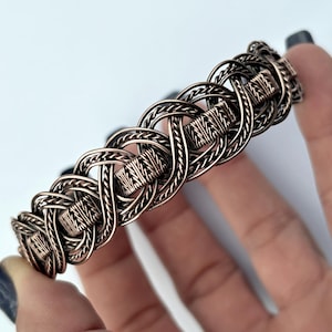 May include: A copper wire bracelet with a woven knot design. The bracelet is made of multiple strands of wire that are intertwined to create a complex pattern.