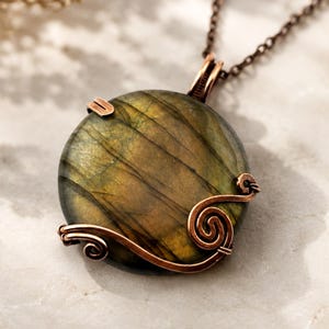 May include: A round labradorite pendant featuring a dark green and gold iridescent surface, encased in a decorative copper wire wrap with spiral accents. The pendant hangs from a dark copper-toned metal chain, showcasing a polished finish.