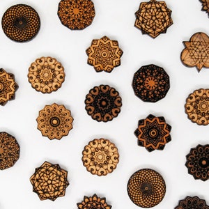 以下が含まれることがあります： 様々な幾何学模様のレーザーカットされた木製のマンダラデザイン16個のセット。マンダラは茶色と黒で、複雑なディテールが施されています。