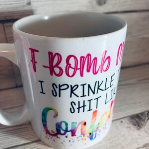 May include: White ceramic coffee mug with a pink design that says "I bomb I sprinkle shit like confetti".