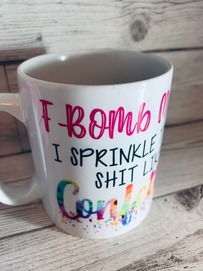 May include: White ceramic coffee mug with a pink design that says "I bomb I sprinkle shit like confetti".