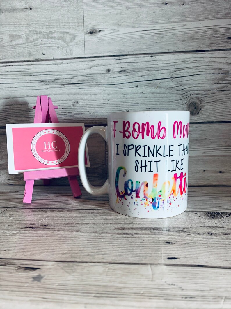 May include: White ceramic mug with a pink and black design. The mug says "I bomb my shit like confetti".