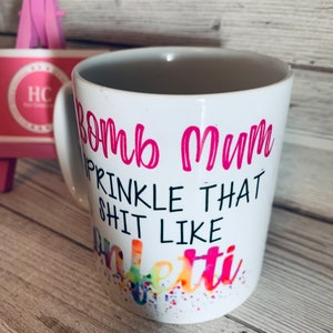 May include: White ceramic mug with a pink design that says "Bomb Mum Sprinkle That Shit Like Confetti".