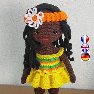 May include: A handmade crochet doll with dark skin, black curly hair, and a yellow dress. The doll has a flower in its hair and is wearing yellow shoes. The dress has orange and green stripes.