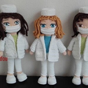 May include: Three crocheted dolls dressed as nurses wearing white coats, pants, and hats. Each doll has a different colored hair and is wearing a face mask.