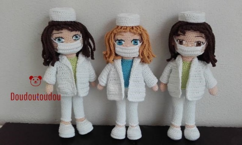 May include: Three crocheted dolls dressed as nurses wearing white coats, pants, and hats. Each doll has a different colored hair and is wearing a face mask.