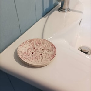 May include: A white ceramic soap dish with a pink floral design and four drainage holes.