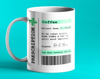 Op de afbeelding: Een witte keramische koffiemok met een groen receptlabel waarop "Coffee" en "To be taken orally FOUR TIMES A DAY or until mood improves" staat. Het label bevat ook een handtekening met "Dr C Bean" en een barcode.