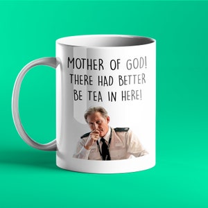 Op de afbeelding: Een witte keramische mok met een zwart-witte afbeelding van een man in politiekostuum. Op de mok staat de tekst "MOTHER OF GOD! THERE HAD BETTER BE TEA IN HERE!" gedrukt.