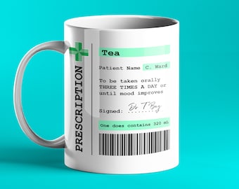 Op de afbeelding: Een witte keramische mok met een groen receptlabel waarop 'Thee' en 'Patiëntnaam C. Ward' staat. Het label bevat ook instructies om de thee drie keer per dag oraal in te nemen of totdat de stemming verbetert. Het label is ondertekend door 'Dr T Bag' en geeft aan dat 'Een dosis 320 ml bevat'.