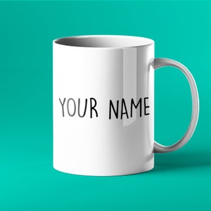 K&ouml;nnte beinhalten: Eine wei&szlig;e Keramiktasse mit einer schwarzen Aufschrift, die "YOUR NAME" lautet.