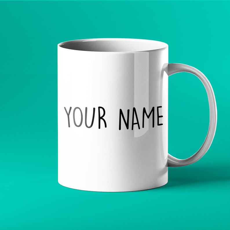 K&ouml;nnte beinhalten: Eine wei&szlig;e Keramiktasse mit einer schwarzen Aufschrift, die "YOUR NAME" lautet.