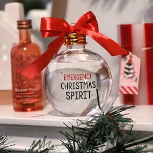May include: A clear glass bauble with a red ribbon and bow. The bauble has the text "EMERGENCY CHRISTMAS SPIRIT" printed on it.