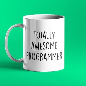 Puede incluir: Taza de café de cerámica blanca con texto negro que dice "Totally Awesome Programmer".