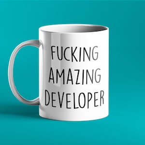Könnte beinhalten: Weiße Keramik-Tasse mit dem Text "FUCKING AMAZING DEVELOPER" in schwarzen, fetten Buchstaben. Die Tasse hat einen gebogenen Henkel und steht vor einem türkisfarbenen Hintergrund. Ein humorvolles Geschenk für einen Softwareentwickler.