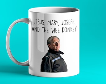 Könnte beinhalten: Eine weiße Keramiktasse mit einem Schwarzweißbild eines Mannes in Polizeiuniform. Der Text "Jesus, Maria, Josef und der kleine Esel" ist auf die Tasse gedruckt.