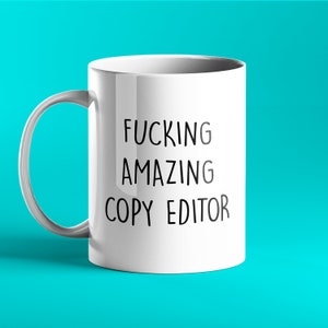 Könnte beinhalten: Eine weiße Keramik-Kaffeetasse mit schwarzem Text, der "FUCKING AMAZING COPY EDITOR" lautet.
