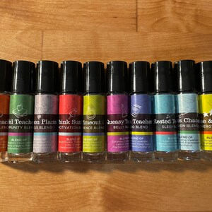 May include: Ten small glass bottles with black roll-on tops and colourful labels. Each bottle has a different name and blend of essential oils. The names include "Happy Teacher", "Community Blend", "Think Plans", "Sum Time Out", "Queasy Belly Blend", "Teacher Blend", "Rested Sleep", "Chaos & Shine", and "Energy Blend".
