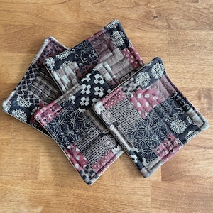 May include: Three quilted fabric pot holders in a patchwork design with black, brown, and burgundy colors. The pot holders have a cream-colored border.