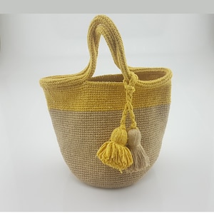 Puede incluir: Un bolso de mano de crochet de color amarillo y beige con dos borlas que cuelgan de las asas.