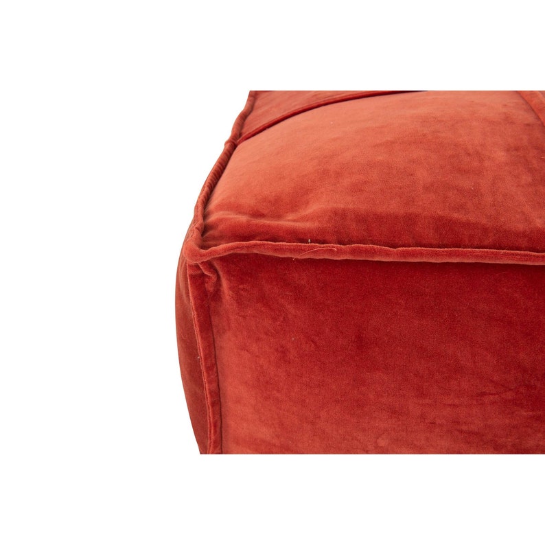 May include: A large, square, red velvet ottoman with a tufted top and a stitched seam around the edges.