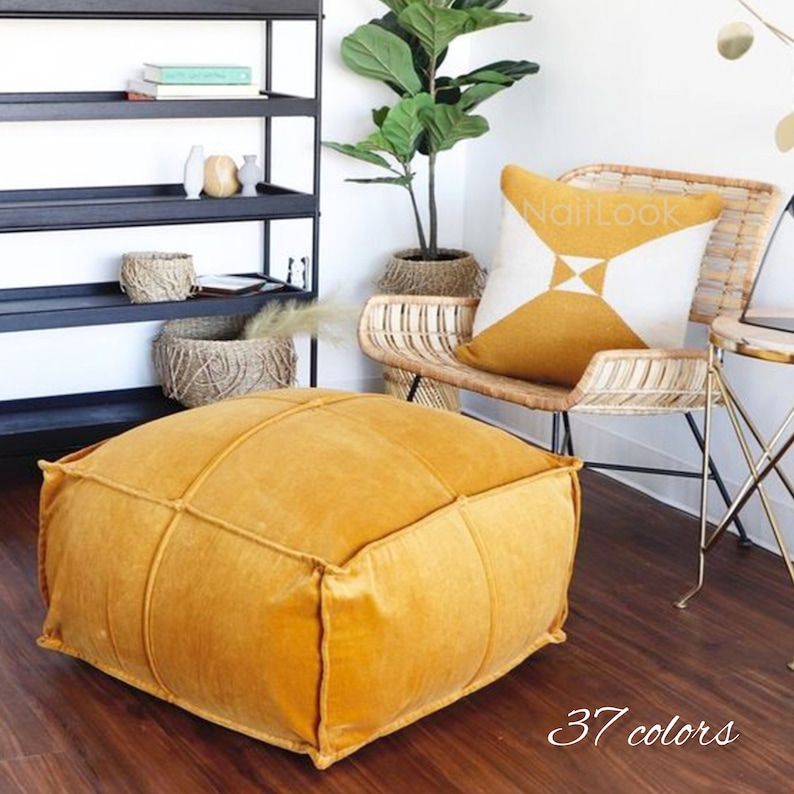 May include: A mustard yellow square pouf ottoman with a tufted design. The pouf is sitting on a wooden floor. The text "37 colors" is written on the floor in front of the pouf.