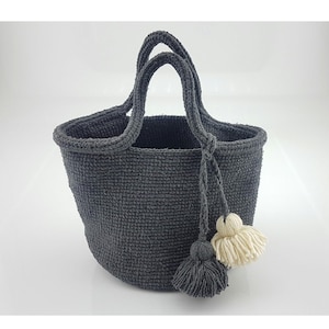 May include: A gray crocheted tote bag with two handles and two tassels. One tassel is white and the other is gray.