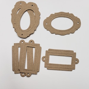 May include: A collection of die-cut cardboard frames in various shapes. The frames are in shades of brown and beige, including oval, rectangular, and ornate designs. Each frame has small holes for hanging or attaching.