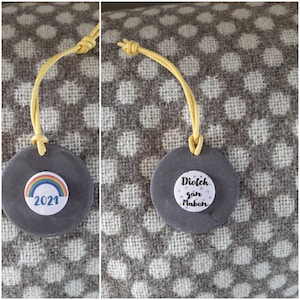 May include: A gray slate circle with a white circle on it that says "2021" and has a rainbow design. The slate circle is attached to a yellow cord.