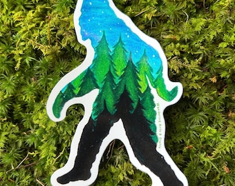 May include: A die-cut sticker shaped like a Bigfoot silhouette featuring a gradient design that transitions from a black base to a forest of green pine trees and a bright blue starry night sky at the top, with the text Wandering Arts & Crafts.