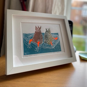 Puede incluir: Una impresión enmarcada de una ilustración de linóleo de dos patos grises nadando en un estanque azul. La impresión está titulada "Grey Ducks - 4/8/17" y firmada "Diane Aspin".