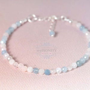 May include: A delicate bracelet made with light blue and white gemstone beads. The bracelet has a silver clasp and extender chain.