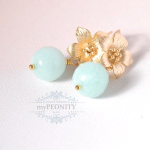May include: Gold earrings with two small flower charms and a light blue round bead on each earring.