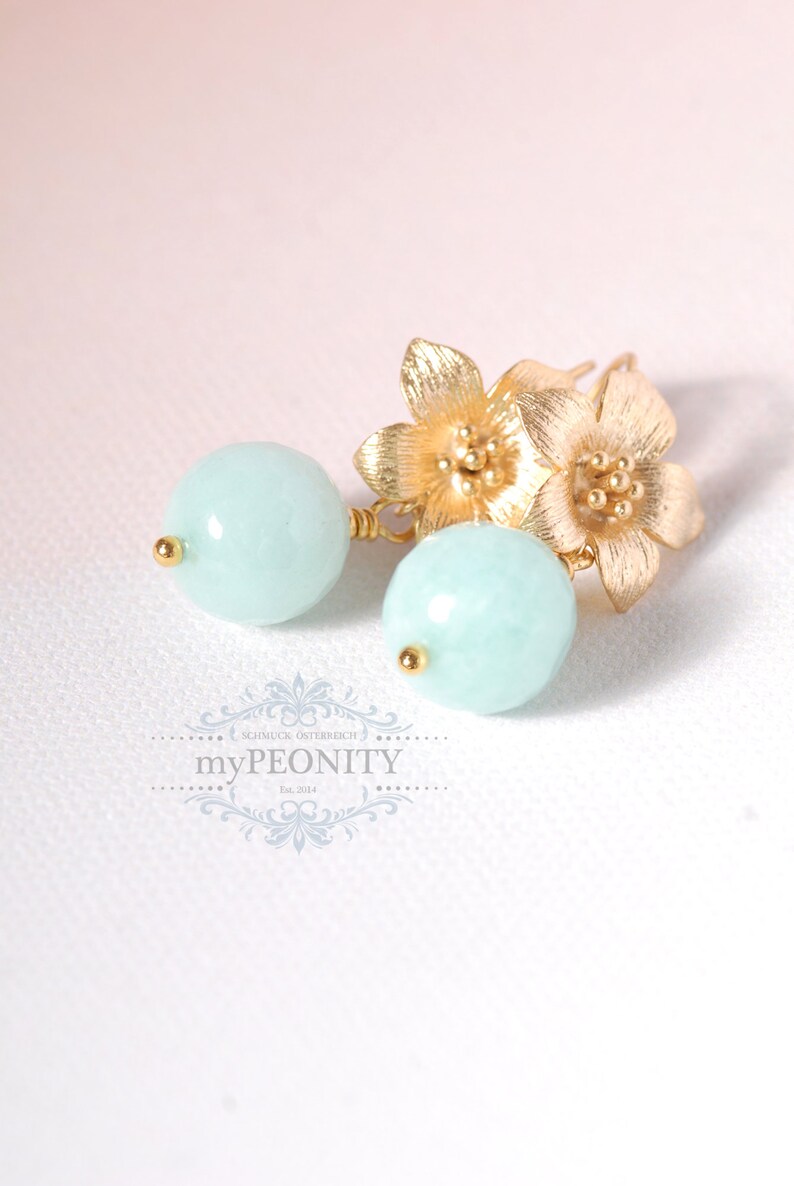 May include: Gold earrings with two small flower charms and a light blue round bead on each earring.