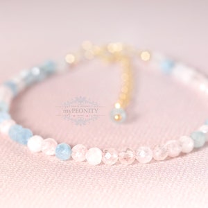May include: A delicate bracelet made with light blue and pink gemstone beads. The bracelet has a gold clasp and is strung on a clear elastic cord.