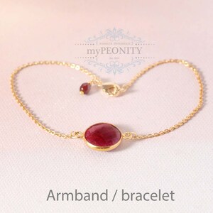 Peut inclure: Un bracelet en chaîne dorée avec un pendentif en pierre rouge. Le bracelet a une fermeture à fermoir mousqueton. Le pendentif est une pierre ronde taillée en cabochon.
